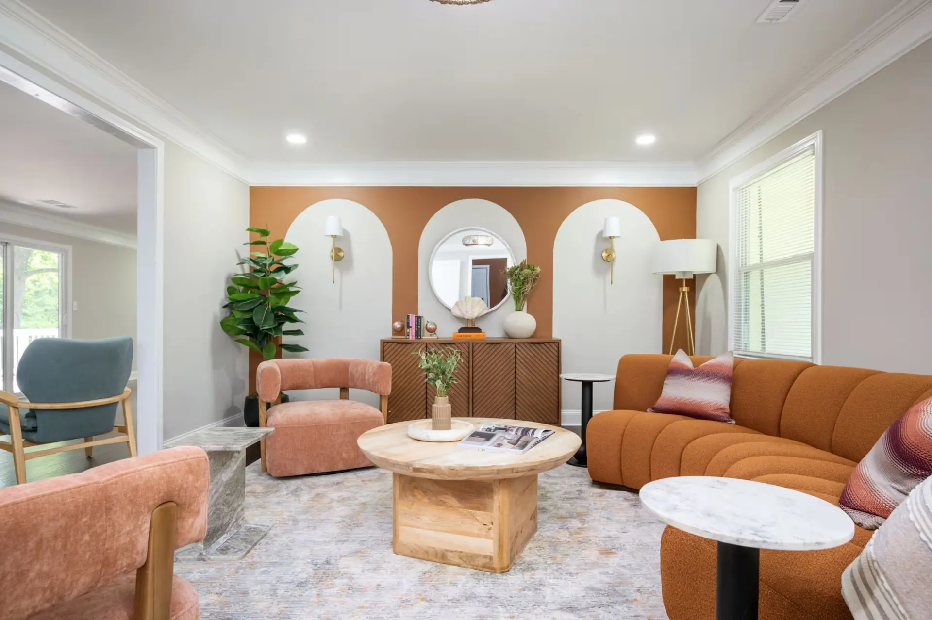 Living room with terracotta arch accent wall, curved rust sofa, and blush chairs