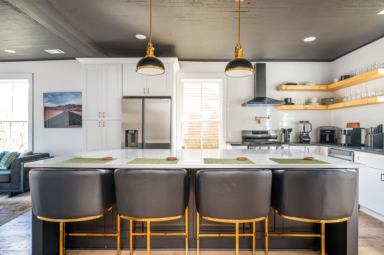 White kitchen with brass pendants, floating shelves, and leather and brass barstools