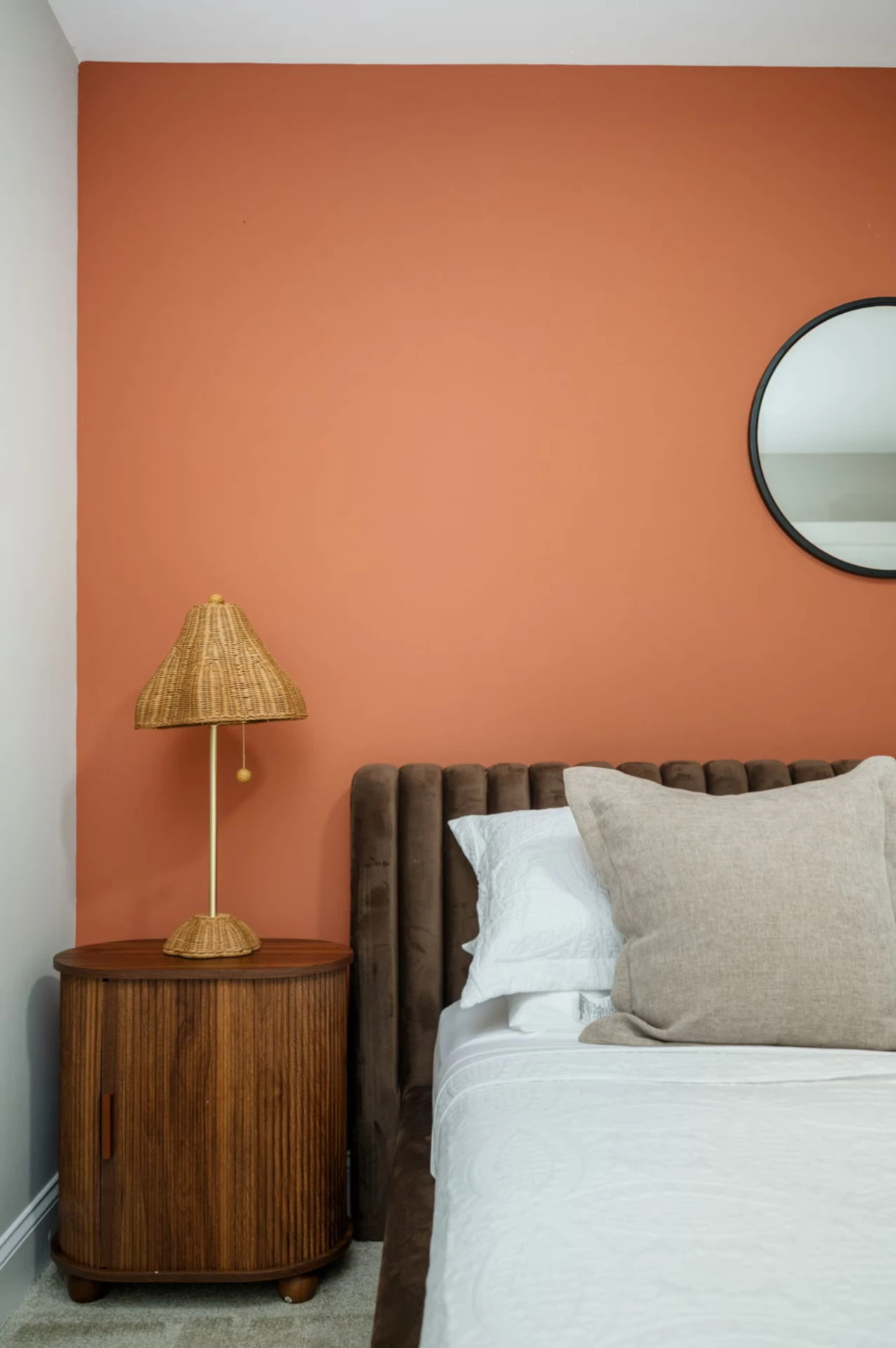Bedroom with terracotta accent wall, velvet channel headboard, and rattan lamp
