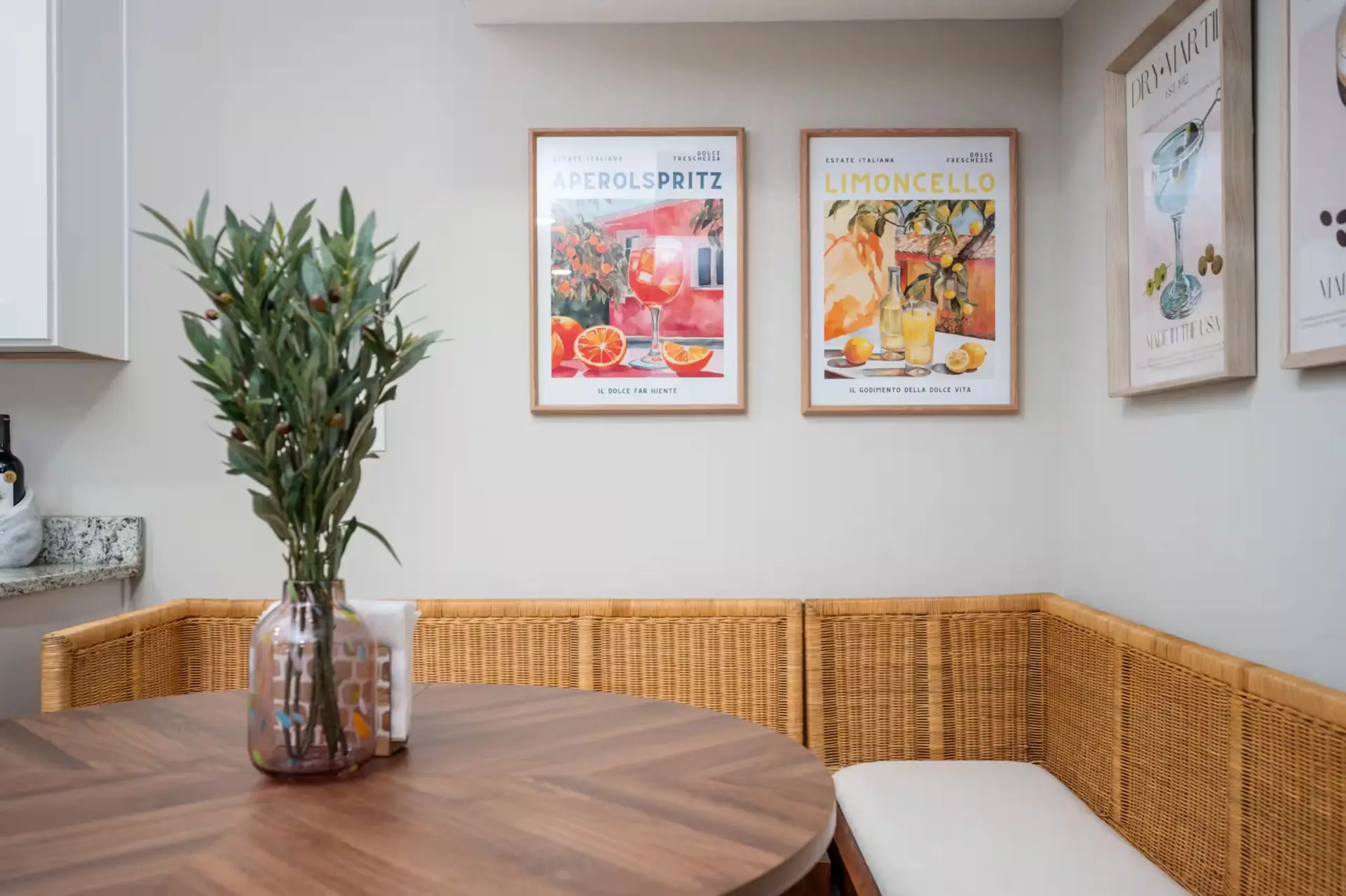 Breakfast nook with rattan banquette, walnut table, and framed cocktail prints