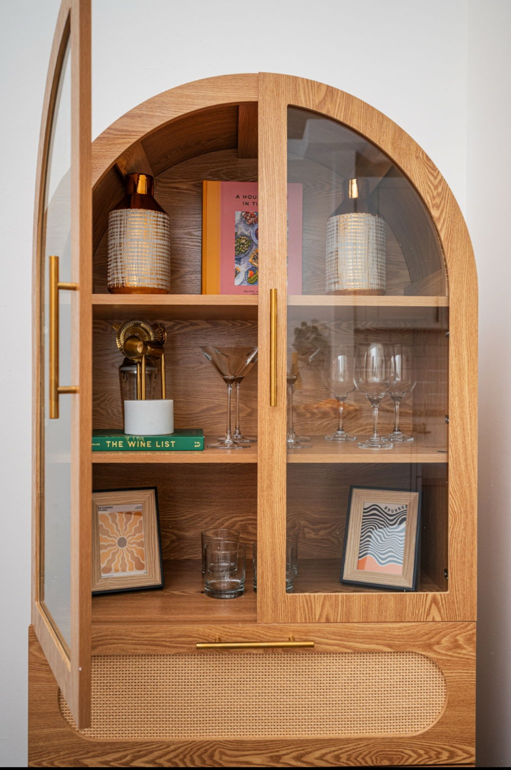 Arched white oak bar cabinet with glass doors, brass hardware, and curated glassware styling