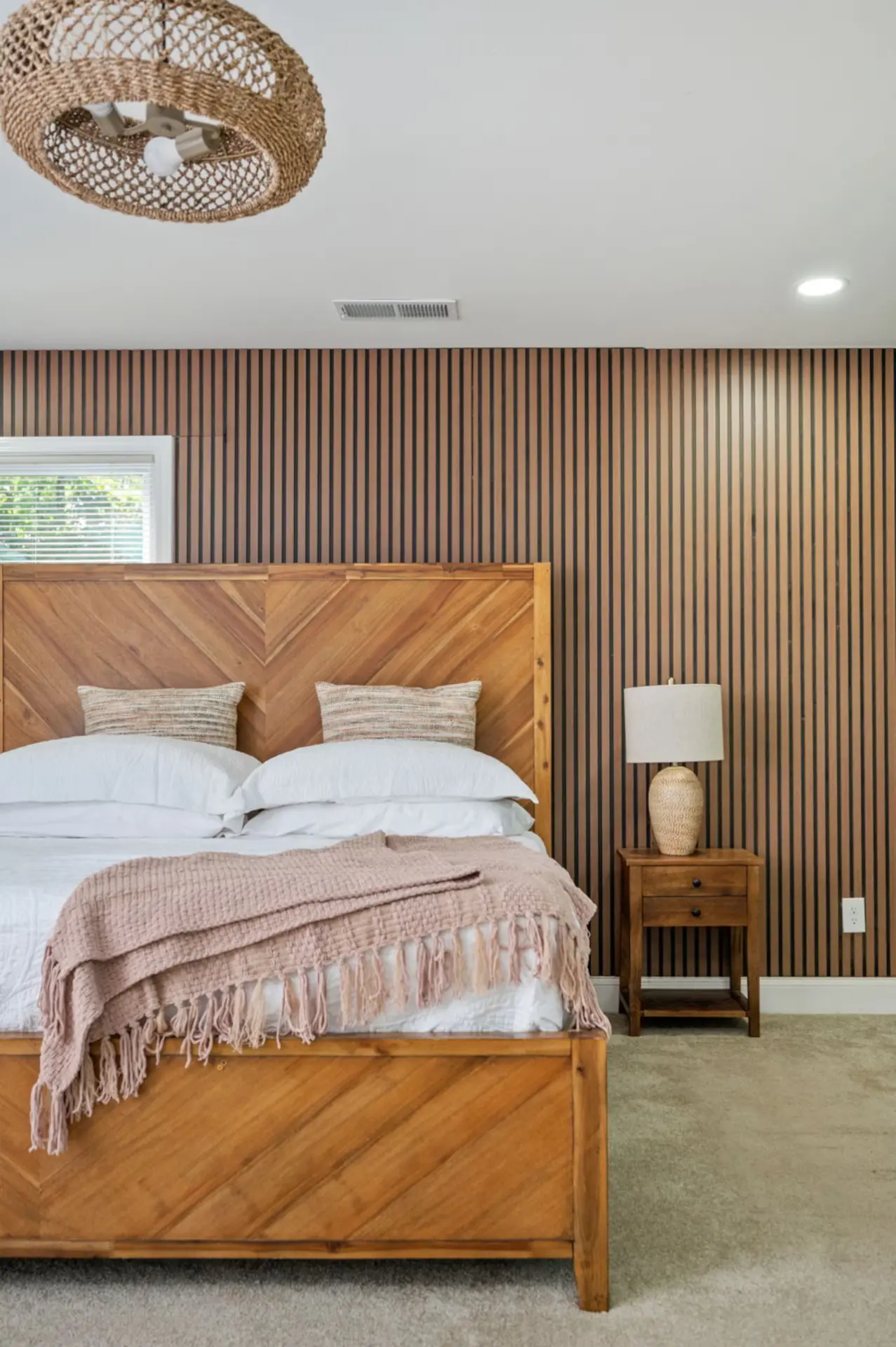 Bedroom with wood slat accent wall, chevron wood bed, and blush throw