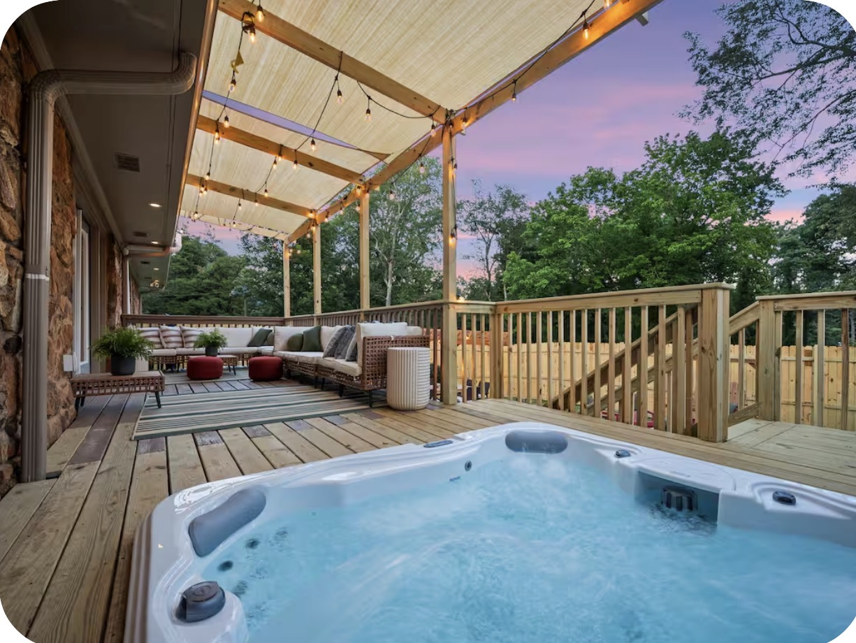 Covered deck with hot tub, sectional lounge and string lights at sunset