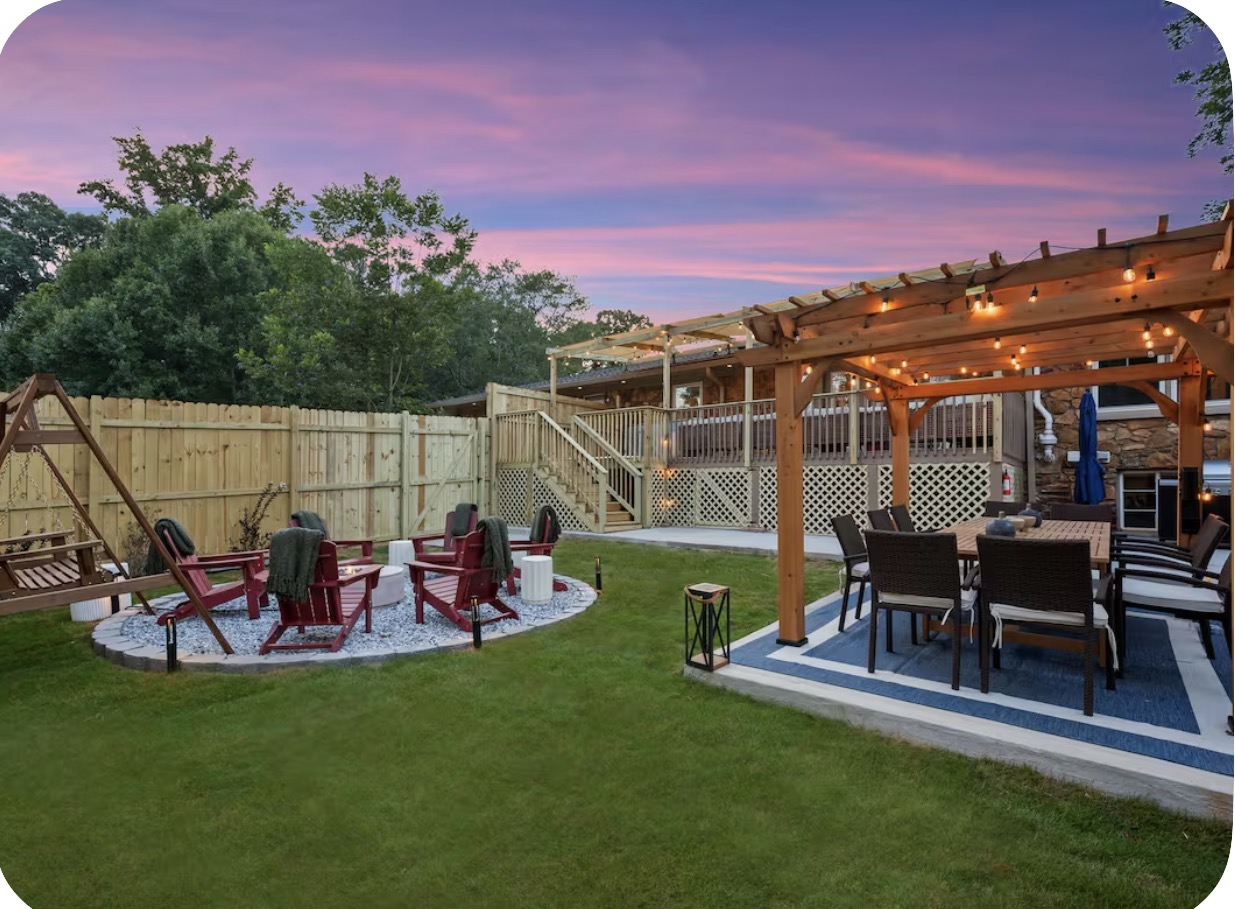 Wide backyard at dusk with pergola dining, fire pit circle, swing set and lawn
