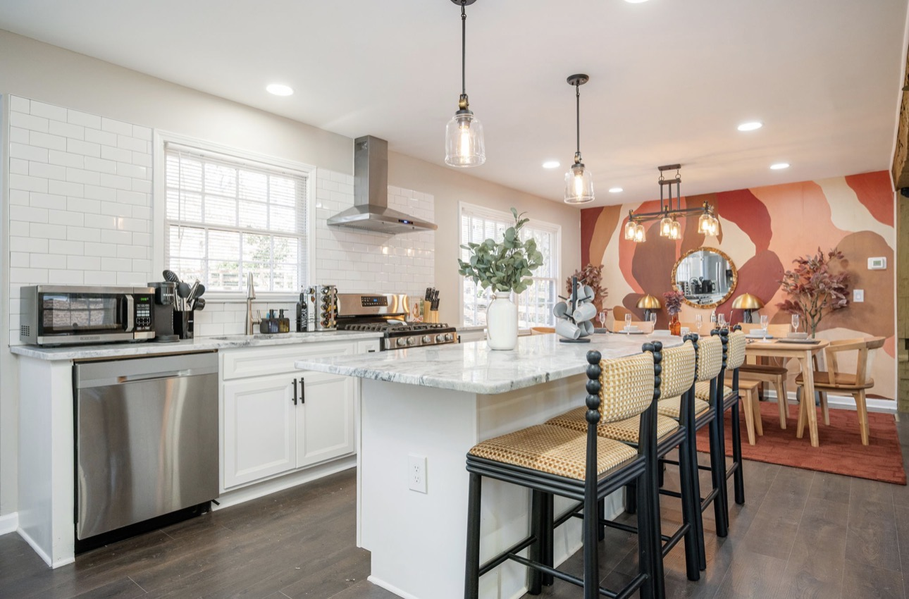 Bright kitchen with marble waterfall island, brass fixtures, and open shelving