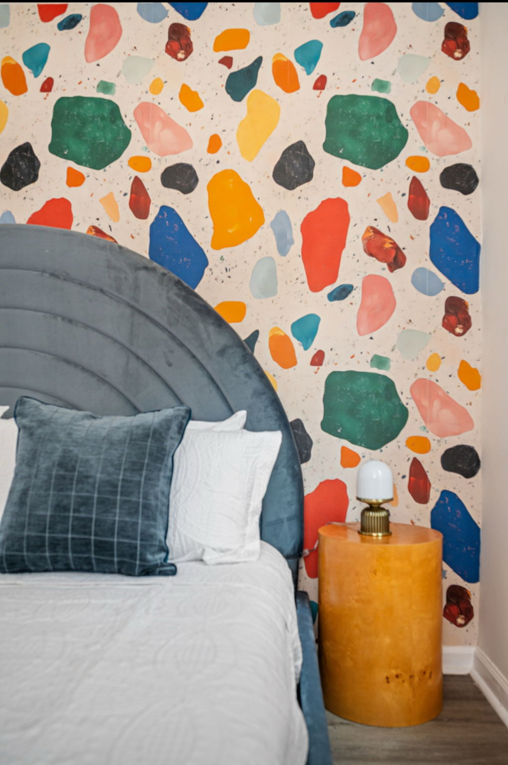 Bedroom with blue arched velvet headboard against colorful terrazzo-style wallpaper