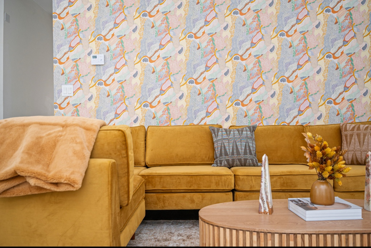Living room with mustard velvet sectional and pastel patterned wallpaper