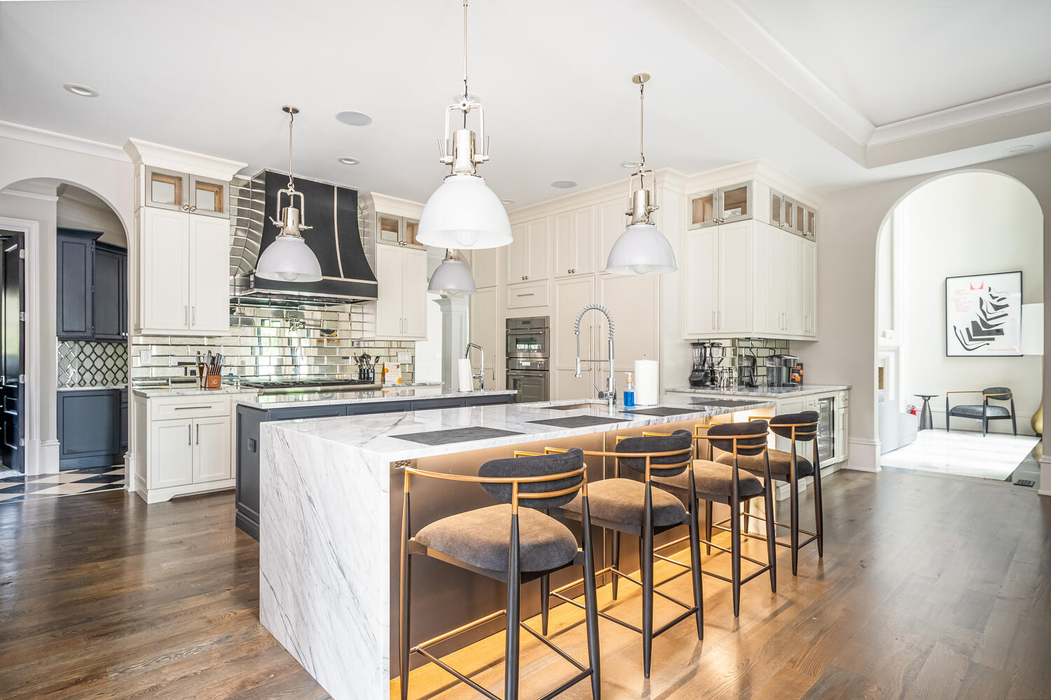 Chef's kitchen with waterfall marble island, mirrored backsplash, and brass barstools