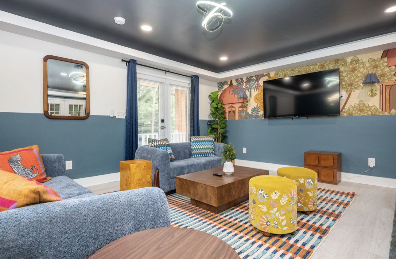 Lower-level lounge with two sofas, mural accent wall, mustard poufs and mounted TV