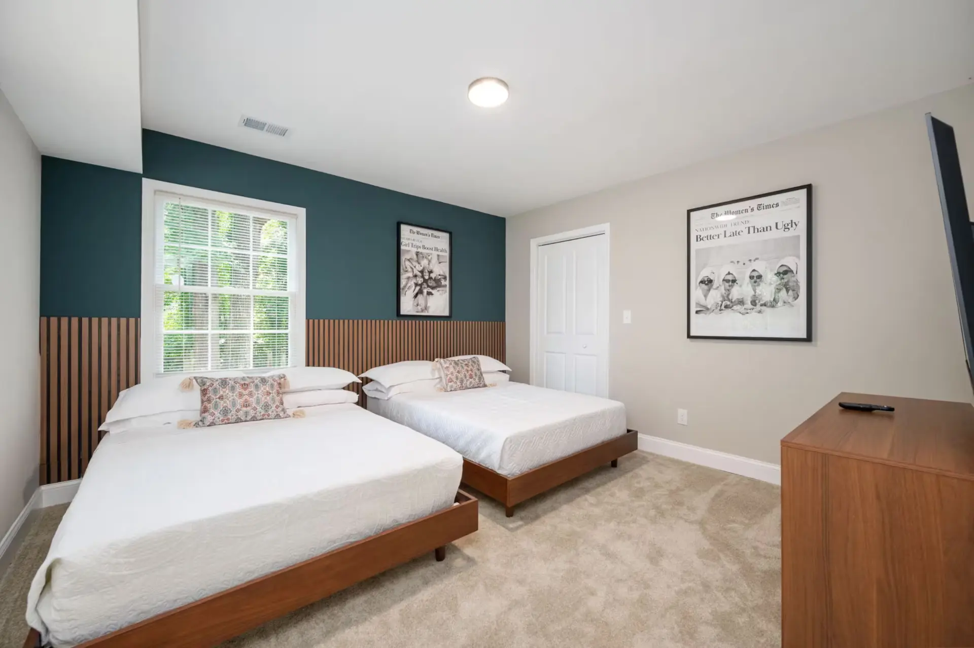 Guest room with two queen beds, teal accent wall, and wood slat wainscoting