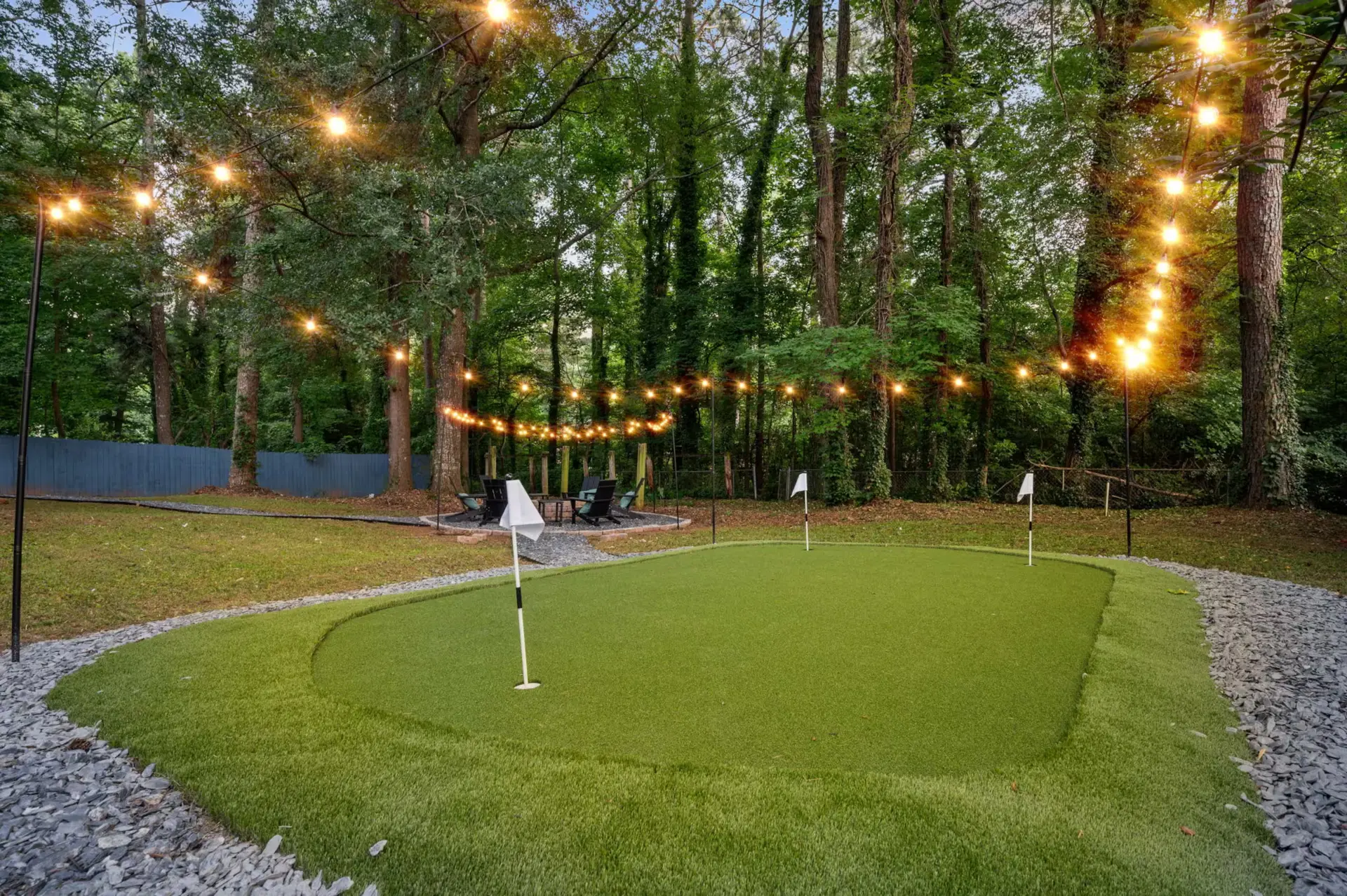 Backyard putting green with string lights and fire pit seating at dusk