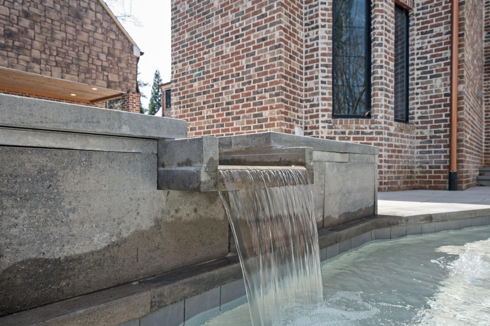 Stone spa waterfall spilling into a pool beside a brick short-term rental exterior