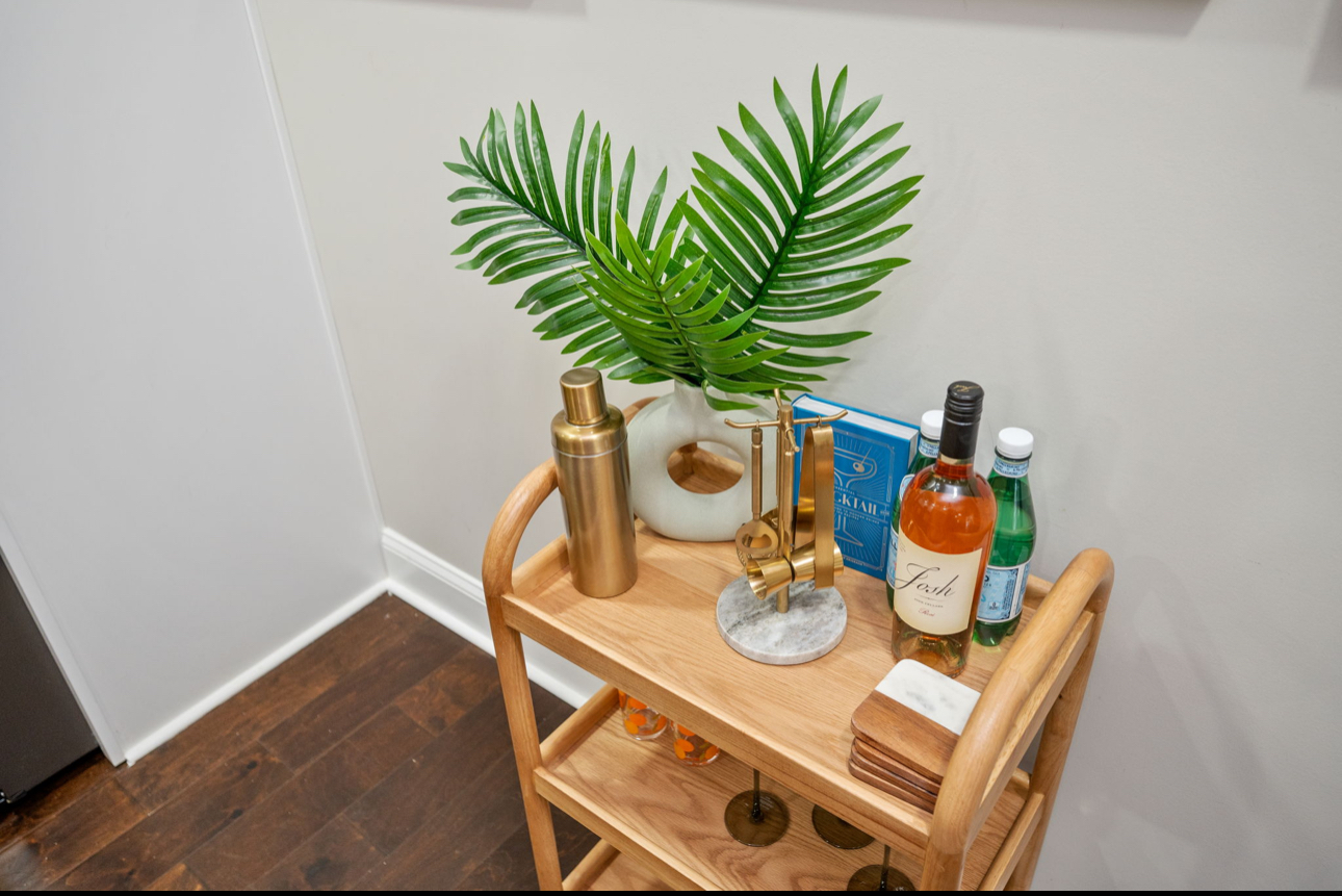 Curated oak bar cart styled with brass shaker, marble coasters, and palm greenery