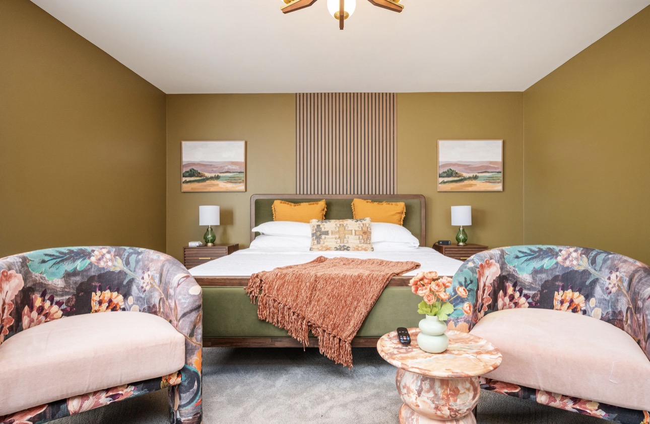 Olive guest bedroom with slat wood accent, mustard pillows, and floral accent chairs