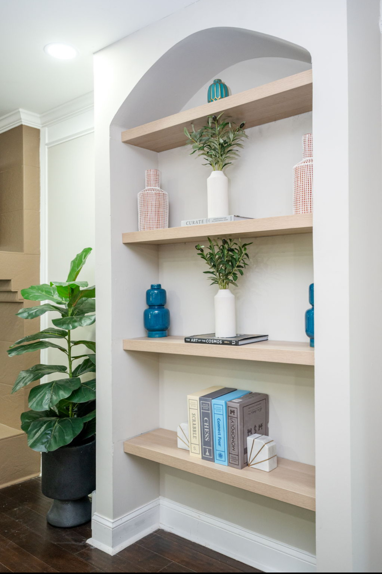 Styled architectural arched shelving with ceramic vases, olive branches, and game boxes
