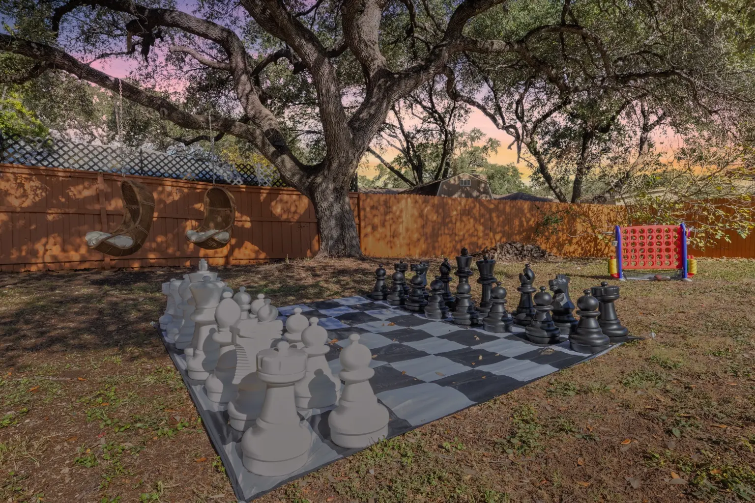 Backyard lawn with oversized chess set under mature trees at dusk