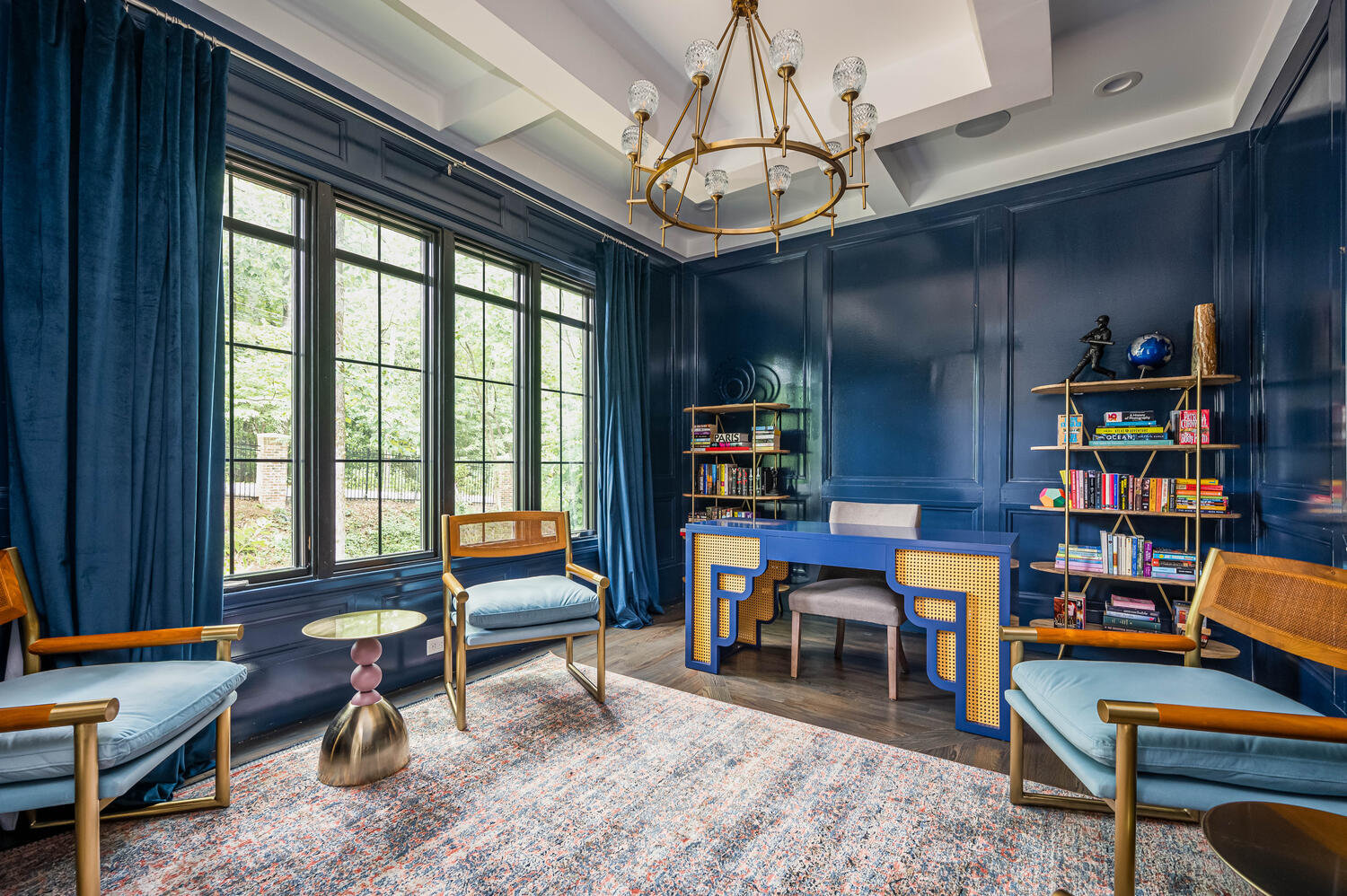 Navy lacquered study with gold chandelier, cane desk, and styled bookshelves