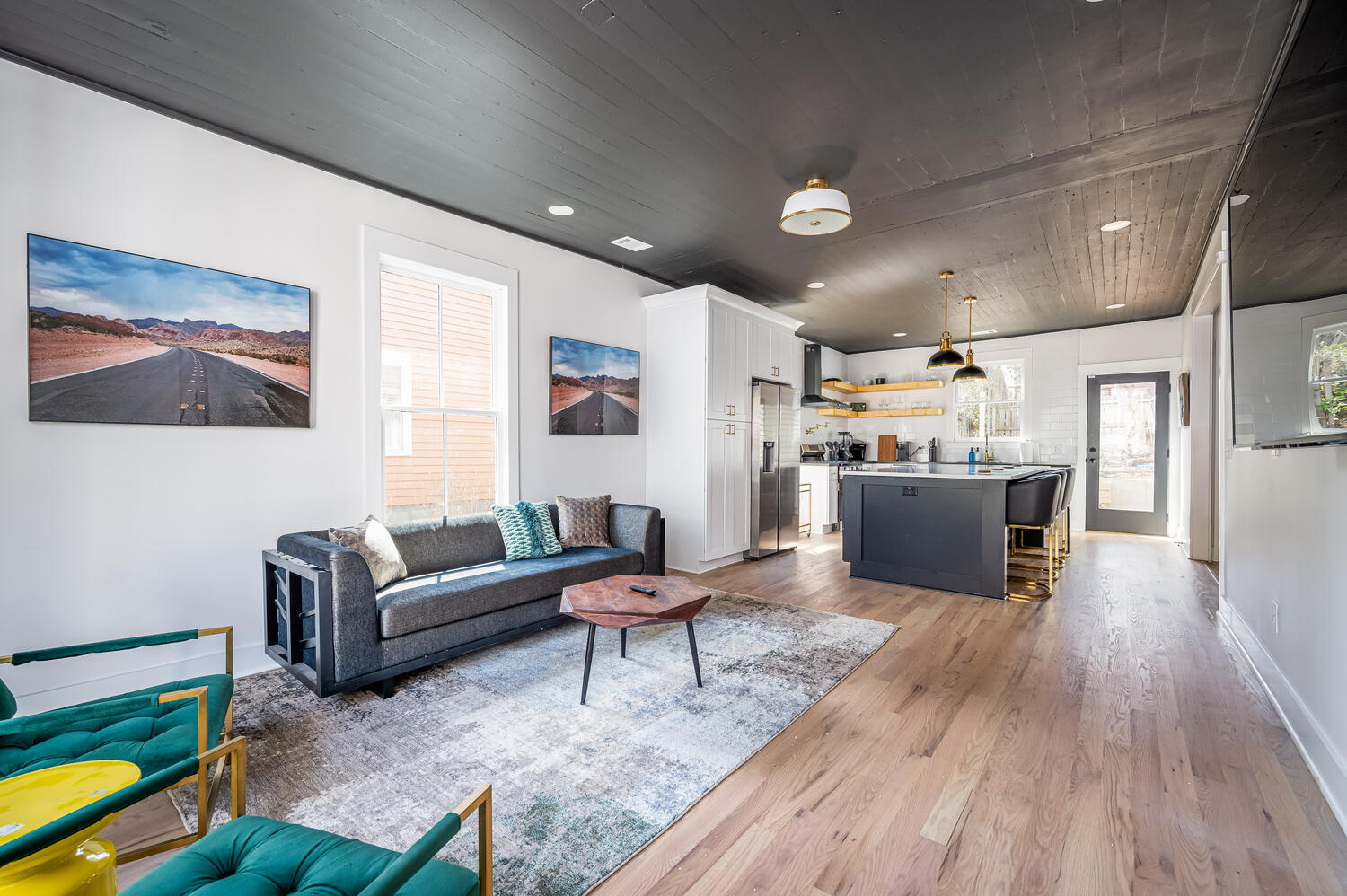 Open-concept living room and kitchen with black shiplap ceiling and emerald accent chairs