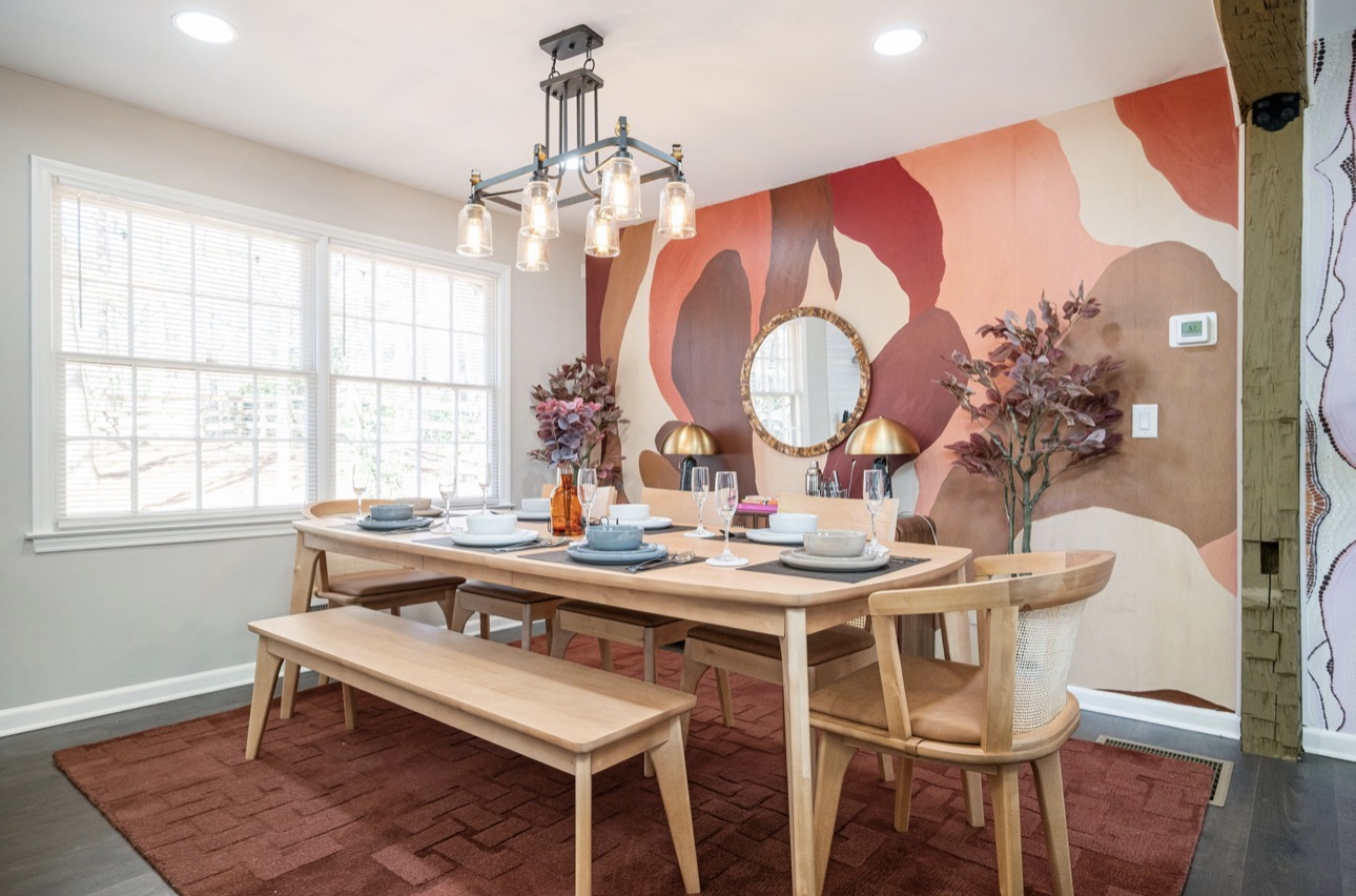 Dining room with terracotta landscape mural, wood table, and woven chairs